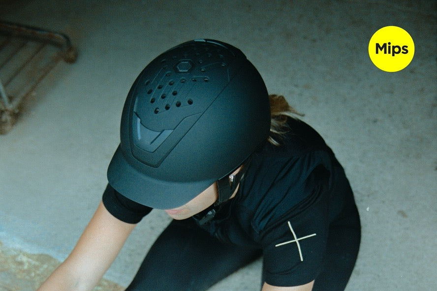 Person wearing a black helmet with 'Mips' logo, stretching on a stone floor.
