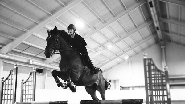 Person riding a horse in an indoor equestrian arena
